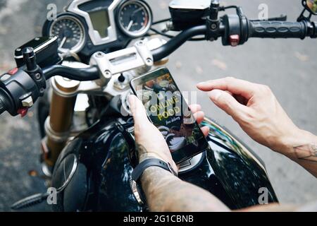 Hände eines Mannes, der auf dem Motorrad sitzt und mit einer mobilen Anwendung Lebensmittel aus dem lokalen Café bestellt Stockfoto