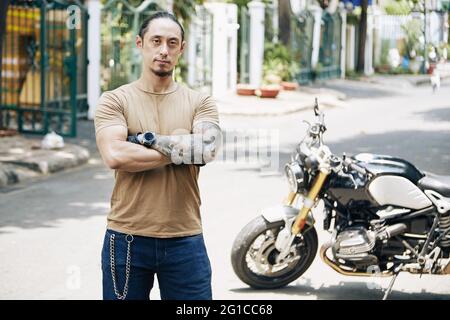 Porträt eines selbstbewussten, seriös fitteren Mannes, der draußen vor seinem Motorrad steht Stockfoto