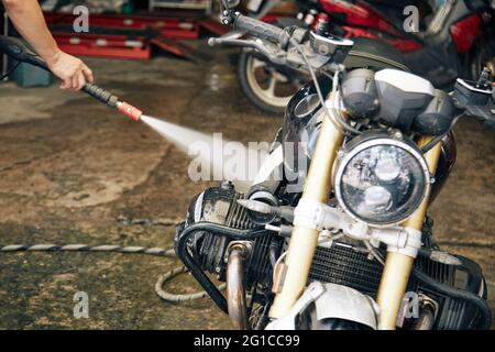 Mann, der sein Motorrad in der Garage mit Wasser spülte, nachdem er auf einer schlammigen Straße gefahren war Stockfoto