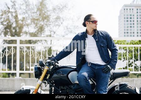 Portrait eines coolen stylischen Mannes in Sonnenbrille, der auf dem Motorrad sitzt und wegschaut Stockfoto