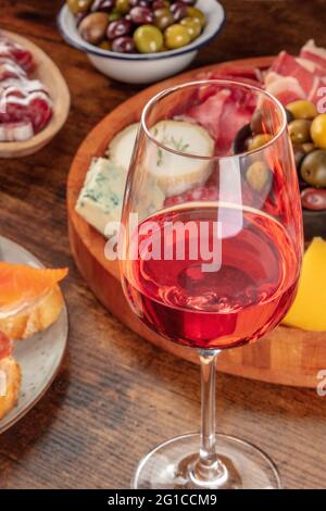 Ein Glas Rosenwein aus nächster Nähe mit einem Käse- und Aufschnitt-Brett im Hintergrund, mit Oliven und Lachs-Sandwiches. Tapas oder Antipasti in einer Bar Stockfoto