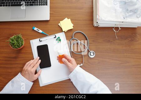 Arzt kommuniziert mit dem Patienten über die Anwendung auf dem Smartphone und sagt ihm, welche Medizin oder Ergänzung zu nehmen, Blick von oben Stockfoto