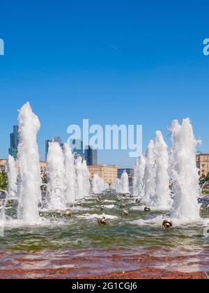 Jets von Springbrunnen an einem sonnigen Tag vor der Kulisse moderner Wolkenkratzer und einem wolkenlosen blauen Himmel. Erholungsgebiet im Victory Park auf Poklonnaya Stockfoto