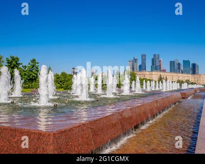 Jets von Springbrunnen an einem sonnigen Tag vor der Kulisse moderner Wolkenkratzer und einem wolkenlosen blauen Himmel. Erholungsgebiet im Victory Park auf Poklonnaya Stockfoto