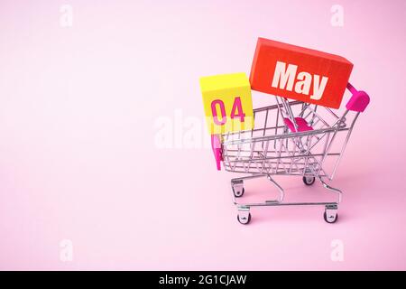 Mai. Tag 4 des Monats, Kalenderdatum. Nahaufnahme Spielzeug-Metall-Warenkorb mit roten und gelben Box innen mit Kalender Datum auf rosa Hintergrund. Feder Stockfoto