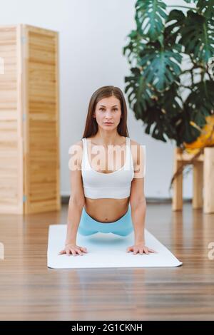 Vorderansicht einer Frau, die komplexe Yoga-Übungen auf dem Boden in einem hellen, sonnigen Zimmer macht. Positiv, Meditation, Konzentration Stockfoto