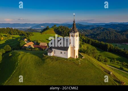 Sveti Andrej, Slowenien - Luftdrohnenansicht der Kirche St. Andreas (Sv. Andrej) bei Sonnenuntergang in der Gegend von Skofja Loka. Sommerzeit in den slowenischen alpen mit c Stockfoto