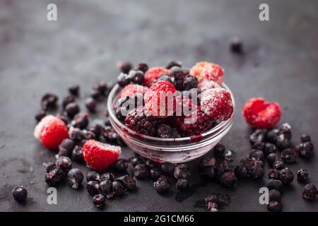 Nahaufnahme von gefrorenen gemischten Früchten und Beeren auf einem schwarzen Tisch gesunde Lebensmittel Vitamine Snack Dessert Stockfoto