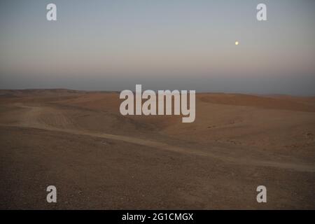 Malerische Aussicht bei Sonnenaufgang oder Dämmerung von Tälern, trockenen Flussbetten und Hügeln des Meyshar in der Nähe von Paran oder Faran in der Negev-Wüste scheint der Mond immer noch. Stockfoto