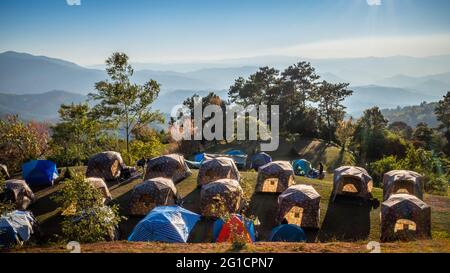 Zelte auf ebenem Gelände mit Bäumen und blauen, von Nebel bedeckten Bergen. Stockfoto