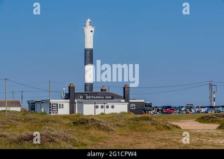 Das Britannia Inn mit Prople saß draußen und genoss die Sonne und einen Drink mit dem New Lighthouse im Hintergrund in Dungeness, Kent, England, Großbritannien. Stockfoto