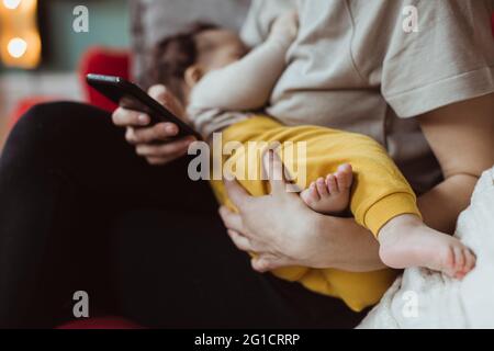 Mittelteil der Mutter mit Baby Junge mit Smartphone im Wohnzimmer Stockfoto