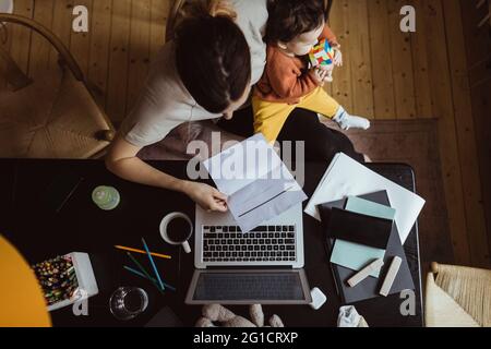 Direkt über der Aufnahme einer Geschäftsfrau beim Lesen eines Dokuments mit einem Kleinkind, das zu Hause arbeitet Stockfoto