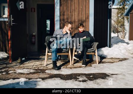 Männliche und weibliche Unternehmer diskutieren über Tablet, während sie vor dem Ferienhaus sitzen Stockfoto