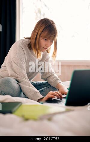 Teenager-Mädchen tippen auf Laptop, während Hausaufgaben zu Hause Stockfoto