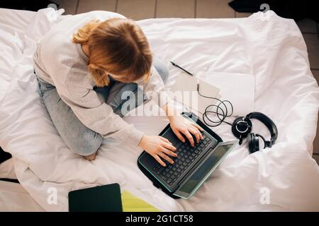 Mädchen macht Hausaufgaben, während mit Laptop im Schlafzimmer zu Hause Stockfoto