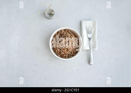 Schale aus Buchweizen auf grauem Betongrund in minimalistischem Stil. Konzept einer ausgewogenen Ernährung und gesunder Ernährung. Draufsicht. Gesunde vegetarische Speisen, Stockfoto