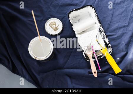 Topf mit weißer Farbe mit Farbe Tray Rolle und Pinsel auf der Oberseite des blauen Drop-Sheet bereit zu malen, in geringer Schärfentiefe mit Farbe geschossen kann Text blu Stockfoto
