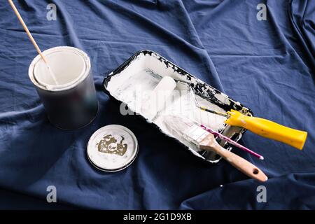 Topf mit weißer Farbe mit Farbe Tray Rolle und Pinsel auf der Oberseite des blauen Drop-Sheet bereit zu malen, in geringer Schärfentiefe mit Farbe geschossen kann Text blu Stockfoto