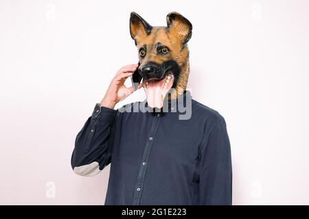 Person mit einer Hundemaske, die auf weißem Hintergrund, Technologie und Kommunikationskonzept am Telefon spricht Stockfoto