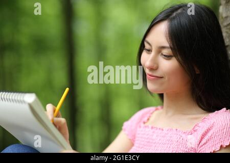 Asiatische glückliche Frau Zeichnung auf Notebook sitzen in einem Park Stockfoto