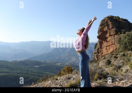 Seitenansicht Porträt einer aufgeregten Frau, die ihren Urlaub feiert und die Arme in den Bergen hebt Stockfoto