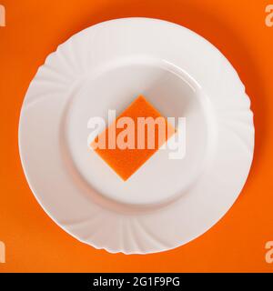 Orangefarbener Teller-Schwamm auf weißem Teller und orangefarbenem Hintergrund Stockfoto