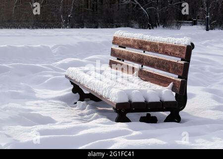 Holzbank im öffentlichen Winterpark nach Schneefall mit Schnee bedeckt Stockfoto