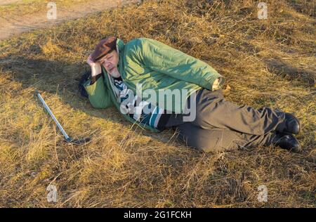 Kaukasischer älterer Wanderer kann sich am Herbstabend kurz am Straßenrand ausruhen Stockfoto