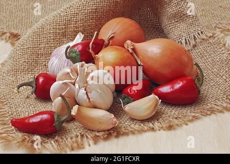 Knoblauch- und Zwiebelzwiebeln, Nelken und Chilischoten auf Sacktuch, volle Schärfentiefe Stockfoto