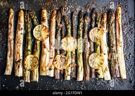 Gebackene weiße, violette und grüne Spargel sprießen Gemüse mit Zitrone, Knoblauch und Käse auf einem dunklen Hintergrund. Food-Fotografie Stockfoto