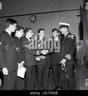 60er Jahre, historisch, Glückwünsche....ein geschmückter Kapitän der Royal Naval, der sich mit einem stolzen jungen Mann die Hände schüttelt und zusammen mit drei anderen männlichen Mitgliedern der Boys Brigade bei einer Preisverleihung in Fife, Schottland, Großbritannien, steht. Die Boys' Brigade wurde 1883 in Glasgow, Schottland, von William Alexander Smith gegründet, um Übung und Spaß mit christlichen Werten zu verbinden. Sie ist die größte christliche uniformierte Jugendorganisation in Großbritannien. Alexander Smiths Einführung von Camping für Jugendliche war im späten 19. Jahrhundert etwas Neues, mit dem ersten BB-Camp in Tighnabruiach im Jahr 1886. Stockfoto