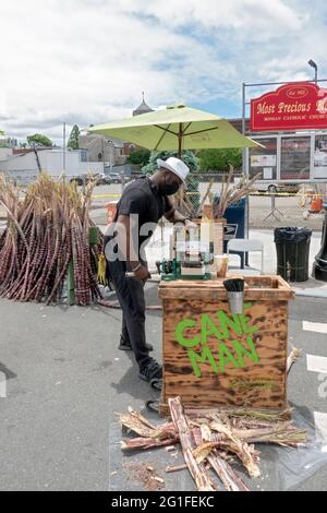 Ein Mann, der auf einer Straßenmesse in Astoria Queens, New York City, frischen Zuckerrohrsaft zubereitet und verkauft. Stockfoto