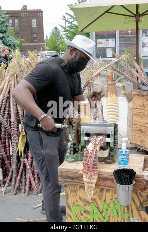 Ein Mann, der auf einer Straßenmesse in Astoria Queens, New York City, frischen Zuckerrohrsaft zubereitet und verkauft. Stockfoto