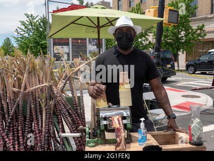 Ein Mann, der auf einer Straßenmesse in Astoria Queens, New York City, frischen Zuckerrohrsaft zubereitet und verkauft. Stockfoto