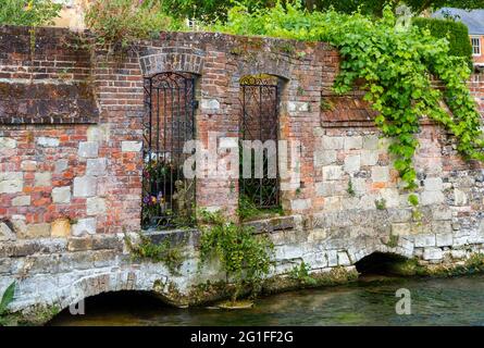 Schmiedeeiserne Tore in einer alten roten Backsteinmauer, die von den Gärten zum Fluss Itchen in den Wehren, Winchester, Hampshire, führt Stockfoto