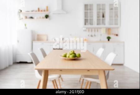 Verschwommenes Foto der klassischen skandinavischen Küche mit hölzernen und weißen Details. Esstisch und helle Möbel Stockfoto