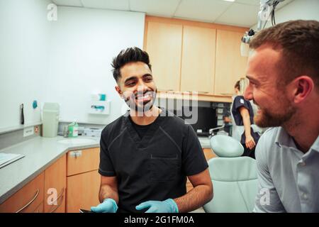 Kaukasische Krankenschwester, die mit einem männlichen Kunden im Arztbüro mit einem digitalen Tablet sitzt Stockfoto