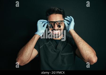 Mixed Race männlichen Arzt lächelt groß, während posiert für Porträt trägt chirurgische Brille und Handschuhe Stockfoto