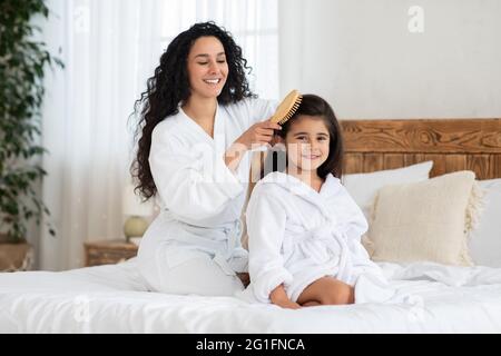 Fröhliche Mutter putzt ihre niedliche Tochter lange lockige Haare Stockfoto