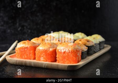 Ein Satz verschiedener Rollen mit Essstäbchen in einer hölzernen Bambusplatte auf einem schwarzen Holzhintergrund. Selektiver Fokus. Stockfoto