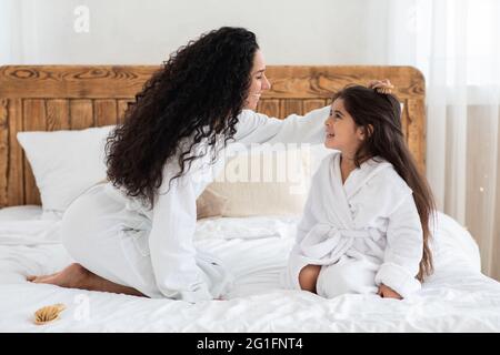 Liebevolle Mutter putzt ihre kleine Tochter lange Haare Stockfoto