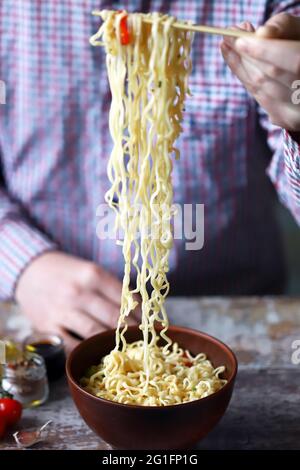 Ein Mann hält Essstäbchen mit chinesischen Nudeln. Chinesische Nudelschale mit Gewürzen. Stockfoto