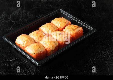 Ein Satz Rollen mit rotem feinkörnigem Tobiko fliegendem Fischkaviar in einer Lieferbox auf schwarzem Holzhintergrund. Selektiver Fokus. Stockfoto