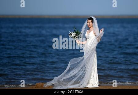 (210607) -- TIANJIN, 7. Juni 2021 (Xinhua) -- EINE Frau im Hochzeitskleid posiert für Fotos in einem künstlichen Strandresort am Hafen von Dongjiang im Binhai New Area im nordchinesischen Tianjin, 5. Juni 2021. Tianjin in Nordchina verfügt über eine reiche Artenvielfalt an einer 153 km langen Küste aus schlammigen Wattflächen. Im Laufe der Jahre hat die Stadt an der Bekämpfung der Umweltverschmutzung und dem Küstenmanagement der Bohai-See gearbeitet, um ihre Feuchtgebiete an der Küste wiederherzustellen, während strengere Maßnahmen zur Landgewinnung ergriffen wurden. Im Jahr 2020 erreichten 70.4 Prozent der Offshore-Gewässer in Tianjin eine Klangqualität unter einem Wechselstrom von drei Jahren Stockfoto