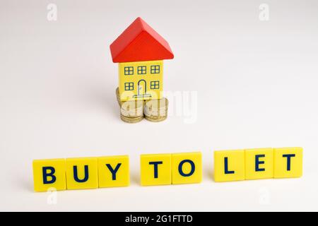 Ein Spielzeughaus, das auf einem Münzstapel sitzt und vor dem die Worte „Buy to Let“ stehen. Stockfoto