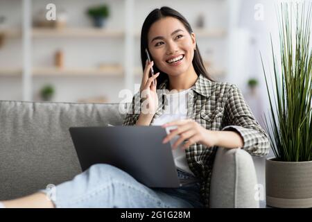 Schöne junge asiatische Frau mit Telefongespräch, mit Laptop Stockfoto