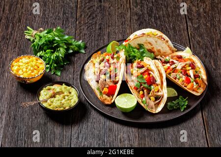 Tacos aus Mehl Tortilla Schalen Füllung mit gegrilltem Hühnerfleisch, Mais, gerösteten Süßkartoffeln Würfel, rotem Pfeffer und Petersilie auf einem schwarzen Teller serviert Stockfoto