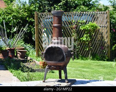 An einem Sommertag in Nottinghamshire ein alter, aus Metall brennender Holzofen im Garten auf einer Gerüstplatte Stockfoto