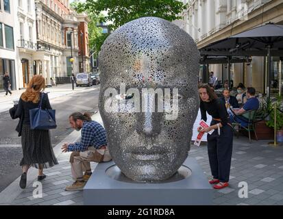 London, Großbritannien. 7. Juni 2021. Das heiße Wetter in London hält die ganze kommende Woche an. Auf Seo Young-Deok, Meditation 626, 2018 sind Aufkleber angebracht, die von der Opera Gallery als Teil des Mayfair Sculpture Trail präsentiert werden, während ein Arbeiter auf dem Sockel sitzt und eine Morgenpause macht. Quelle: Malcolm Park/Alamy Live News.Quelle: Malcolm Park/Alamy Live News. Stockfoto